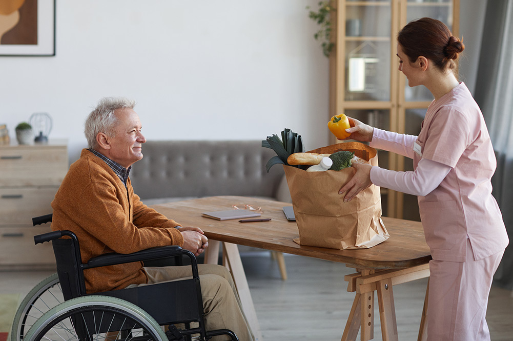 Woman unpacking groceries for senior man in wheelchair
