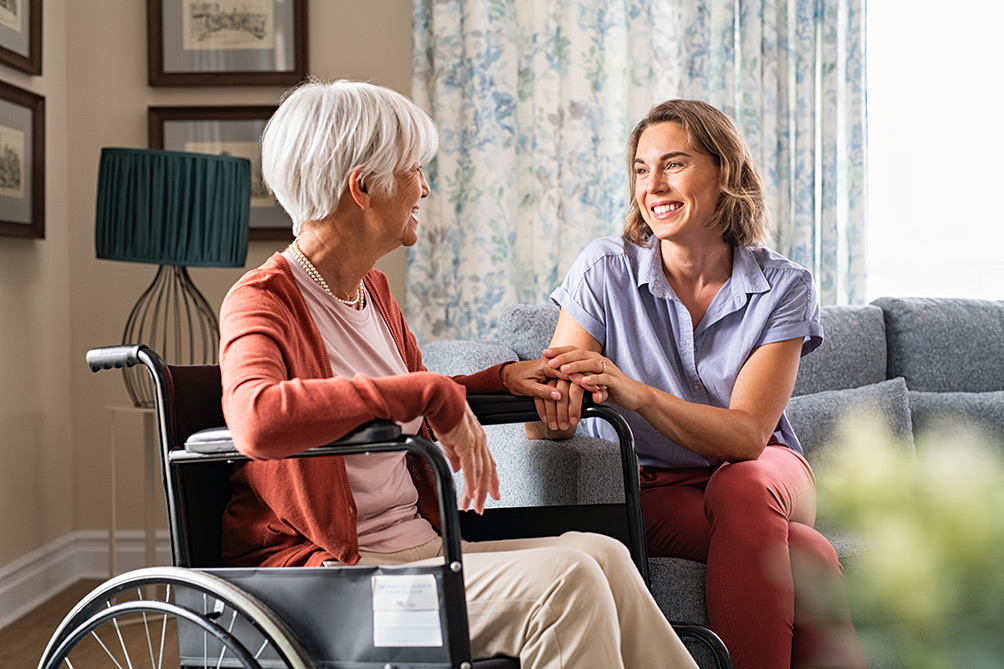 Senior woman in wheelchair chatting with care worker in living room