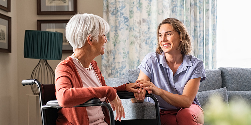 Senior woman in wheelchair chatting with care worker woman in home